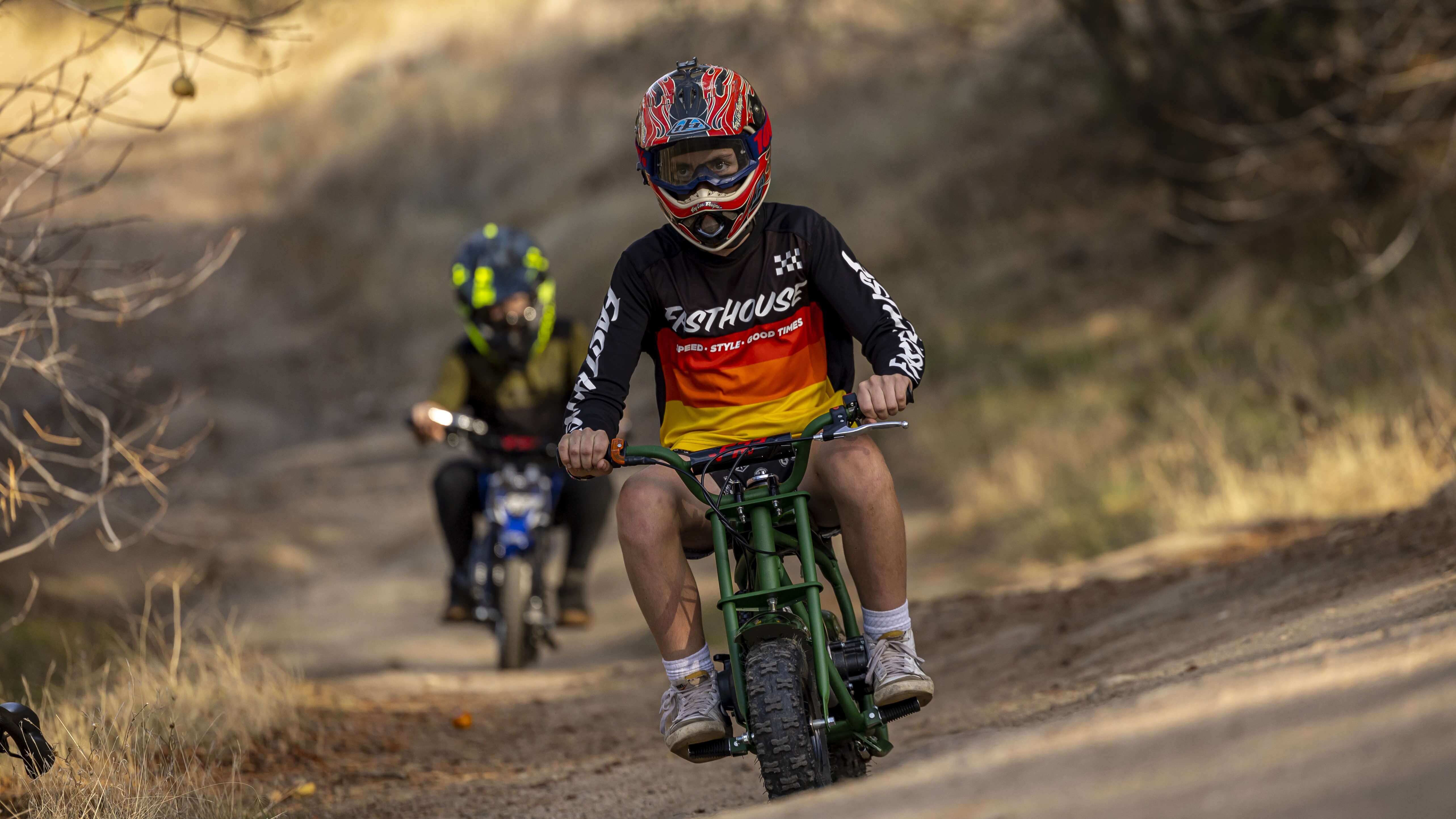 Two kids are riding FRP gas mini dirt bikes on a muddy road.