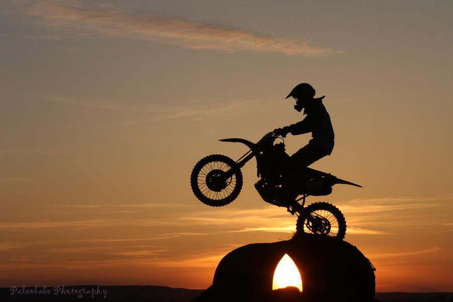 A man is riding a dirt bike, the background is sunset.